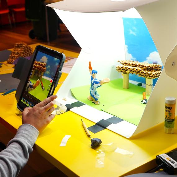 child holding ipad and making a stop motion movie on the table with plasticine characters