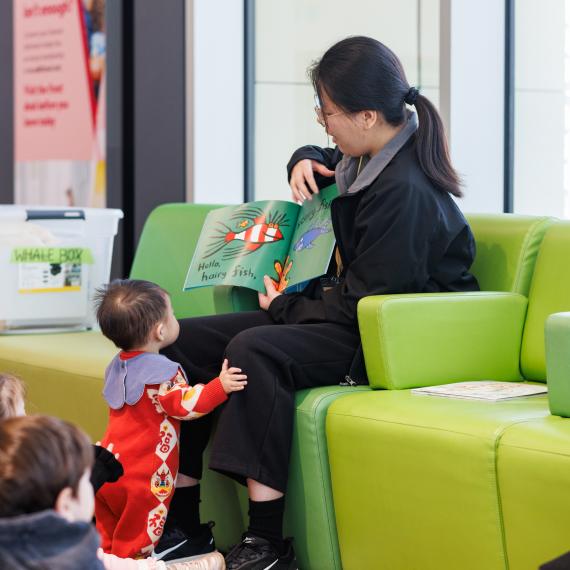 Volunteer reading a book about fish with a child at her knees looking at the book