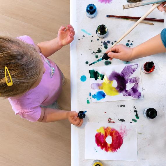 topdown view of an activity table with paints, ink and artwork where a child approaches the table to take part