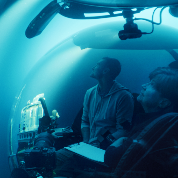 Two pepole in a submersible underwater with a camera